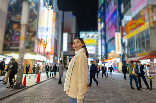 Asian woman crossing street crosswalk with crowd of people during shopping at Shibuya district, Tokyo, Japan at night. Attractive girl enjoy outdoor lifestyle travel city on autumn holiday vacation.