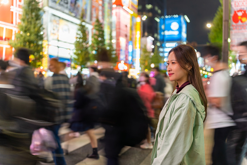 Asian woman shopping and crossing street crosswalk with crowd of people at Shibuya, Tokyo, Japan at night. Attractive girl  enjoy and fun outdoor lifestyle travel in city on autumn holiday vacation.