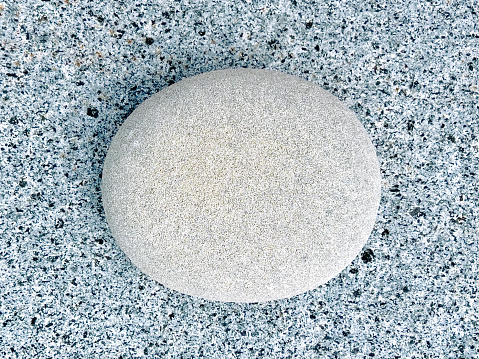 Horizontal high angle extreme closeup photo of a smooth round pale grey granite rock on top of a granite crystal rock surface. Granite Bay, Noosa National Park, Noosa Heads, SE Queensland.