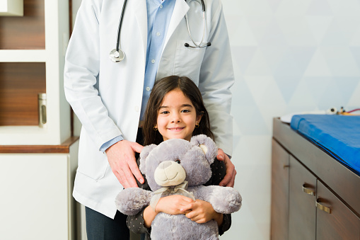 Cute latin little girl smiling while hugging her teddy bear toy after a medical check-up at the pediatrician's
