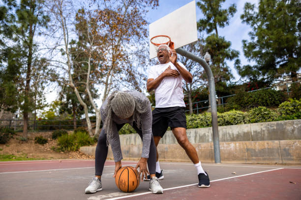 donna nera anziana che dribbla pallacanestro mentre il marito la difende - athlete coach basketball male foto e immagini stock