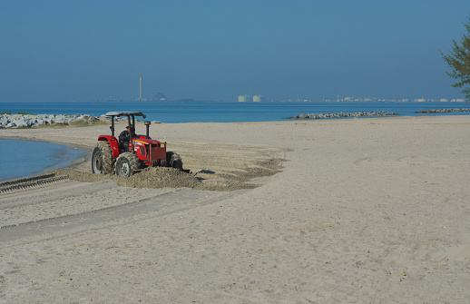 On the seashore, there is sand and sea water.The tractor is plowing and adjusting the sand on the seashore. Captured on January 20, 2023 in Rayong, Thailand.