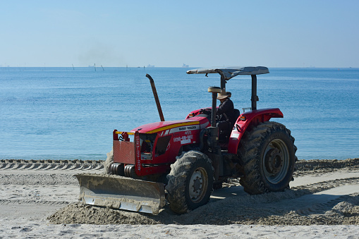 On the seashore, there is sand and sea water.The tractor is plowing and adjusting the sand on the seashore. Captured on January 20, 2023 in Rayong, Thailand.