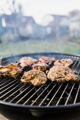 Chicken meat on a hot grill with smoke and flames. The bbq is a round charcoal grill.