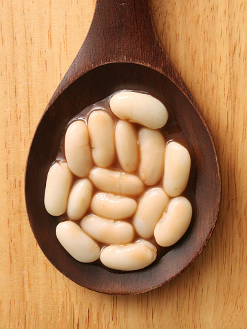 Top view of wooden spoon with boiled beans and sauce on it