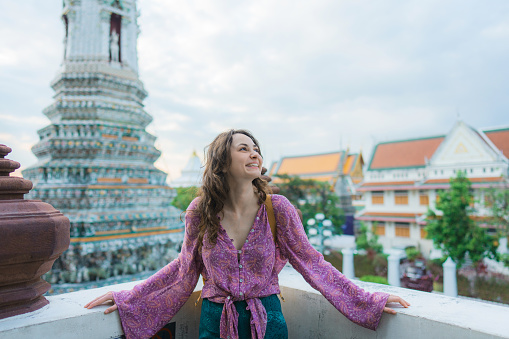 Young Caucasian woman standing on the background of the pagoda of colourful ornate in Wat Arun, Bangkok