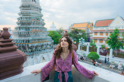 Young Caucasian woman standing on the background of the pagoda of colourful ornate in Wat Arun, Bangkok