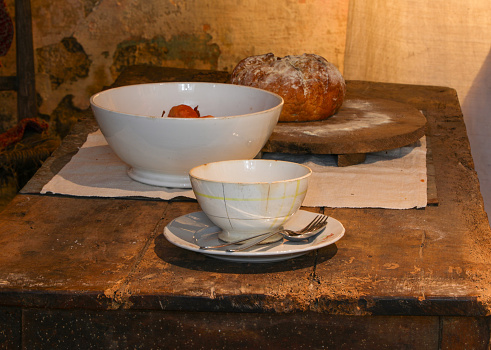 historical reconstruction of an ancient table set with bowl and bread in the old rural kitchen of the poor farm