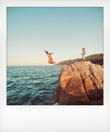 Photo of a young boy and his father jumping off the cliff into the sea