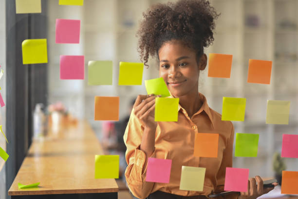 istock Pleasant African American business woman analyzing process schedule, looking at sticky notes on board. Through glass view. 1462493741