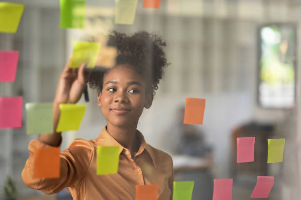 istock Smiling African American female employee analyzing process schedule, looking at board with colorful sticky notes. 1462493745