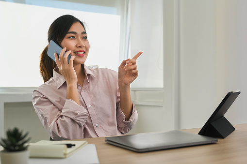 Asian female financial advisor having phone conversation with client and looking aways.