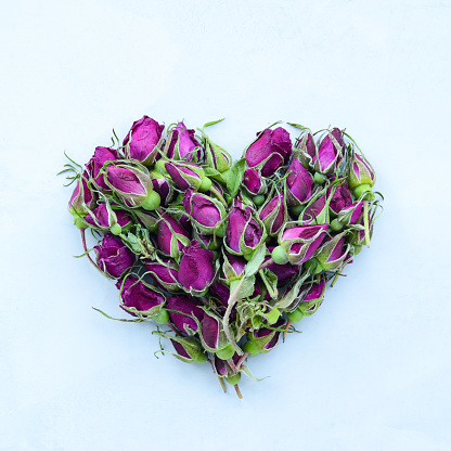 Heart of red roses buds on a light background, flat lay. Flower Valentine. Floral heart shape. Dried Rosehip flowers and buds, love with tea made in flowers