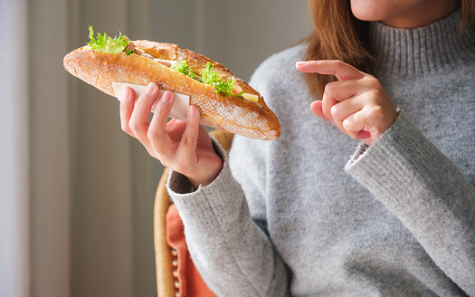 Closeup image of a young woman holding and pointing finger at a piece of french baguette sandwich at home