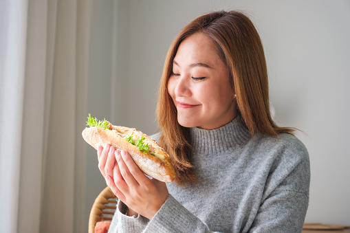 Portrait image of a young woman holding a piece of french baguette sandwich at home