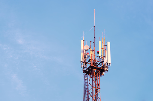 High antenna of mobile communication on the background of the blue sky. Red steel tower frame and cell transmitters