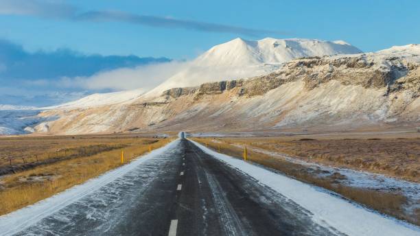 istock Empty road covered in snow with mountains in the background on a sunny day 1462529048