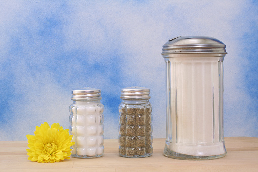 A flower and salt, pepper, and sugar shakers on a blue background on the wooden surface.