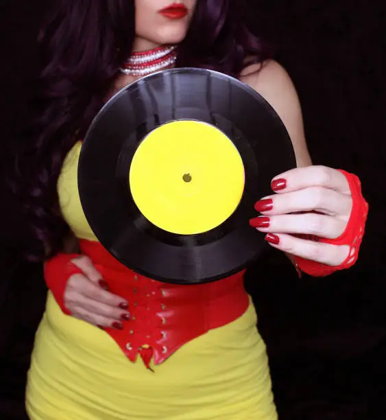 A woman in 1980s yellow clothing holding 45rpm record. Record label painted with yellow paint