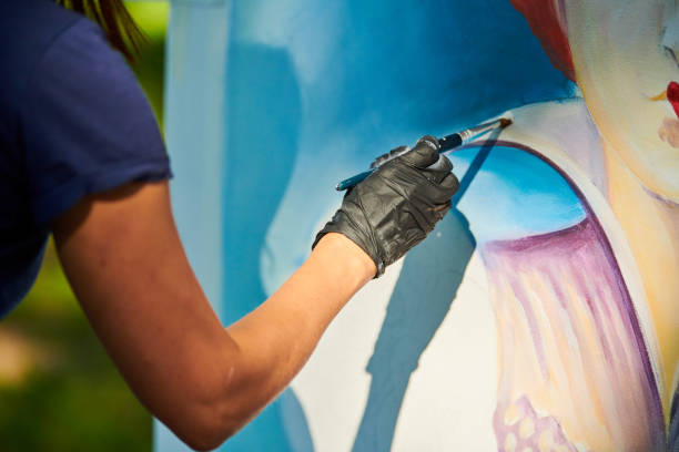 Girl artist hand holds paint brush and draws surreal fairy tale portrait on white canvas Girl artist hand holds paint brush and draws surreal fairy tale portrait on white canvas outdoor art painting festival, paintings art picture process. Woman artist paints atmospheric surreal picture painting-art-product stock pictures, royalty-free photos & images