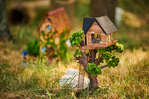 Little dollhouse on front lawn, cute small decorative house on green grass field, environment concept. Forest small doll house in green grass, charming garden decoration for home lawn,