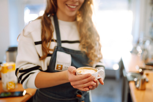 Barista  holds a cup with coffee in his hands. A drawing is drawn on coffee foam. Food and drink concept.