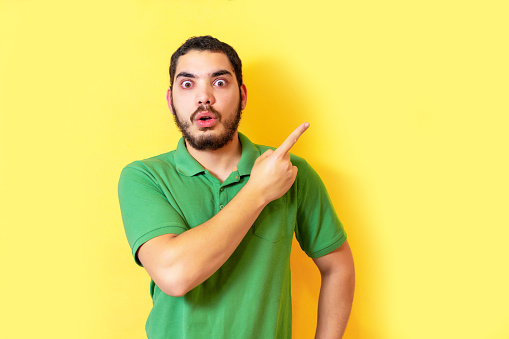 A Middle Eastern Funny surprised bearded male looks with bugged eyes and indicates as shows something, isolated over yellow wall