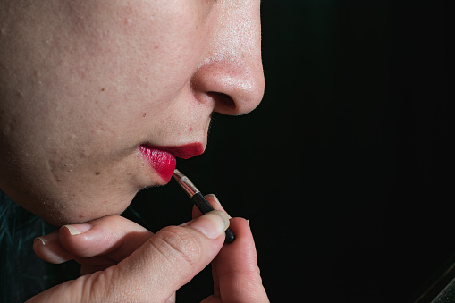 A beautiful Latina woman putting red lipstick on her lips isolated on a dark background