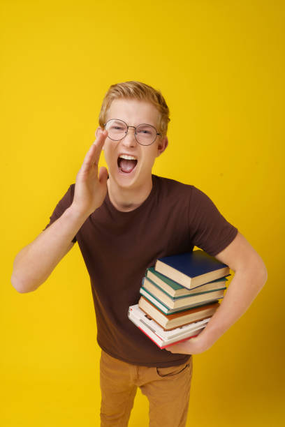 istock College Education Concept. Student Invites Applicants to Study. A Young Man with Books on a Yellow Background. 1462568457