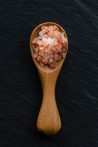 Wooden spoon with a heap of Himalayan salt on black background.