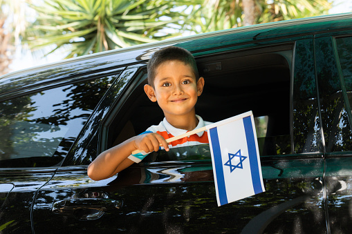 Little Boy in car is holding flag of Israel with a cute smile.