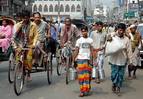A crowd of people walking or riding rickshaws along the street in Dhaka, Bangladesh. This is a typical local life scene in Dhaka, the capital city.