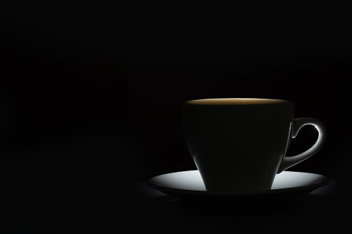 Silhouette of a mug with a warm drink on a black background. Morning coffee.
