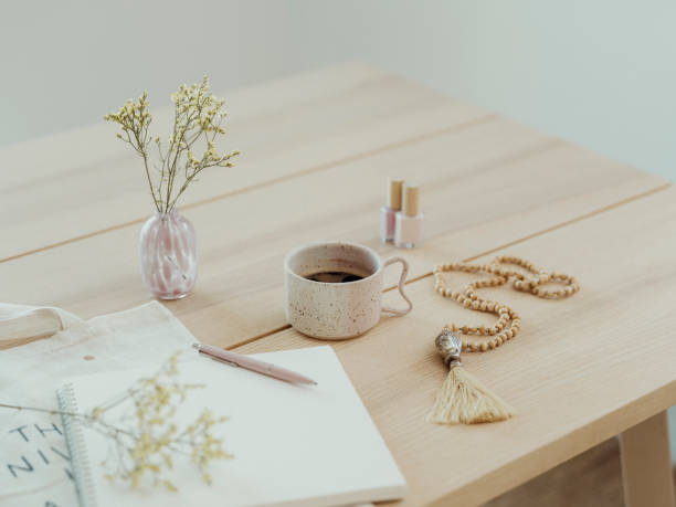 Modern still life at home coffee cup note book zen buddha necklace and pen on table\nBRight photo taken indoors