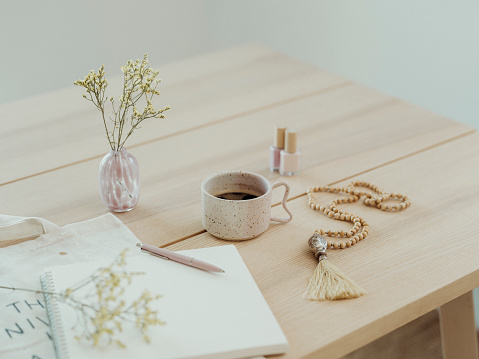 Modern still life at home coffee cup note book zen buddha necklace and pen on table
BRight photo taken indoors