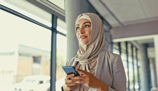Muslim, smile or startup woman with phone in office building for social media, networking or communication. Happy, islamic or girl employee with smartphone for search, online content or internet app