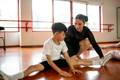 Boy stretching with the help of dance instructor at ballet class