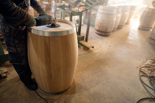 At the wood workshop, a Caucasian male barrel maker, using sander to polish an oak barrel