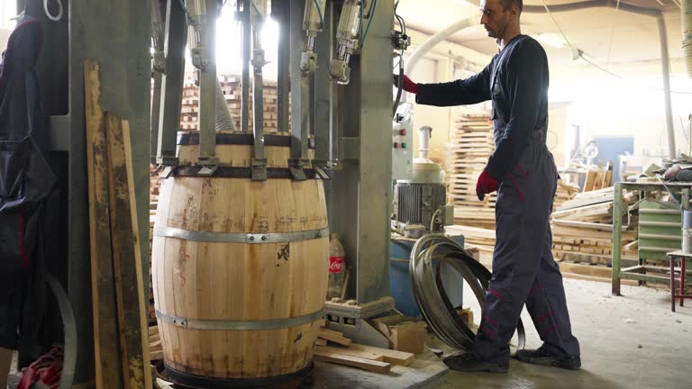 Cooper using machine to clamps wooden steves to form a barrel shape