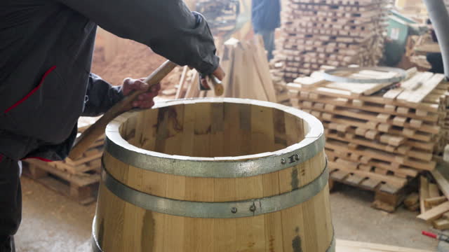 Cooper adjusting metal hoops around an oak barrel with hammer