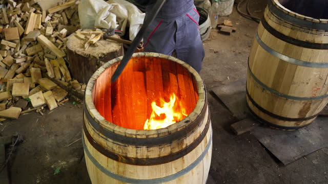 Cooper burning an oak barrel, so the wooden steves become flexible to form a barrel shape