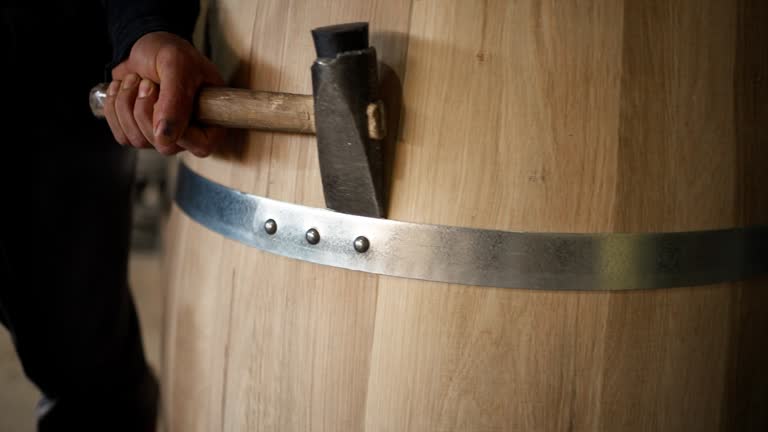 Cooper adjusting metal hoops around an oak barrel with hammer