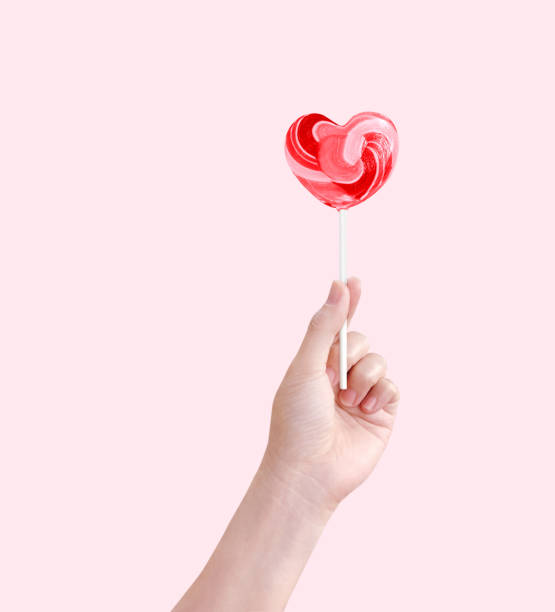 istock Heart shaped lollipop candy in hand isolated on pink background. 1462620616