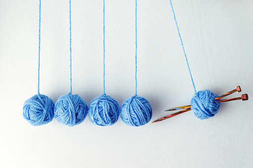 Newton's cradle from balls of blue knitting threads, copy space, creative photo