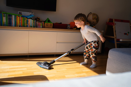 Caucasian toddler boy playing with a vacuum cleaner in the living room