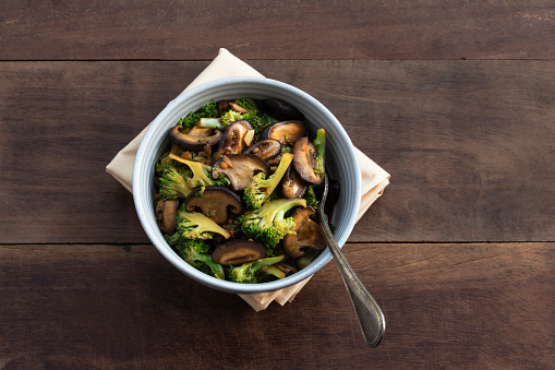 Stir Fried broccoli mushroom in bowl on wood background close up, top view, vegetarian food concept.