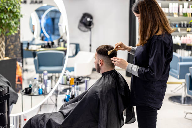 A young man is having a haircut in a barbershop. A young handsome man is sitting in a barbershop and having a haircut by a young female barber. electric razor human hair scissors cutting stock pictures, royalty-free photos & images