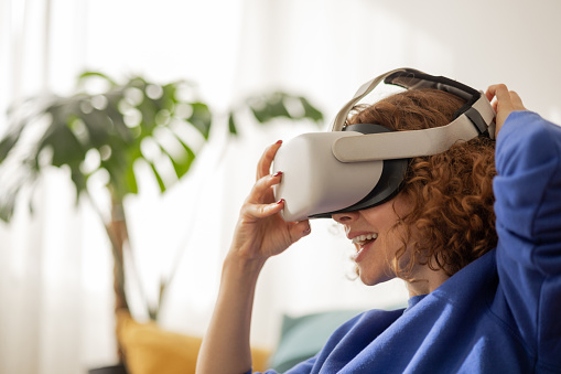 Pretty and happy ginger woman excited to put on VR set and enjoys virtual world