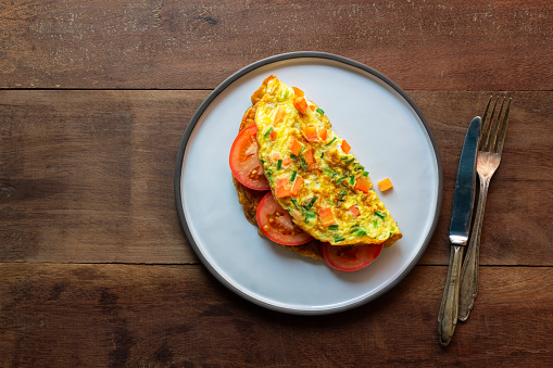 Omelet has tomato in plate isolated on wood background, top view, healthy breakfast food concept.