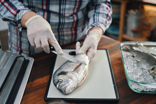 Food Safety - Cleaning and Cutting Sea Bream Fish on Plastic Cutting Board with Food Gloves